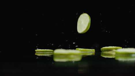 Rings-of-green-lime-sliced-fall-on-the-glass-with-splashes-of-water-in-slow-motion